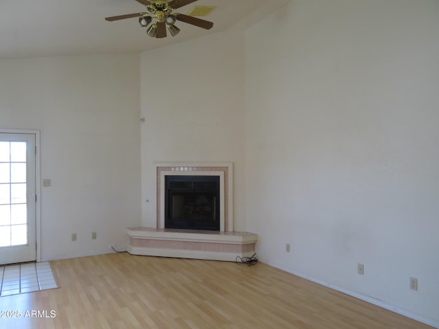 unfurnished living room featuring high vaulted ceiling, a fireplace with raised hearth, a ceiling fan, and wood finished floors
