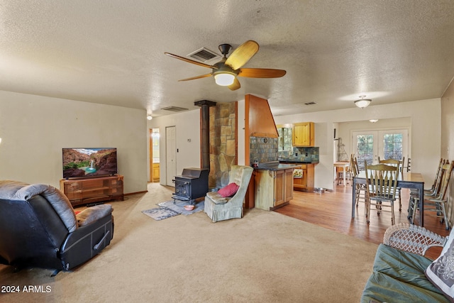 living room with ceiling fan, a wood stove, light hardwood / wood-style floors, and a textured ceiling