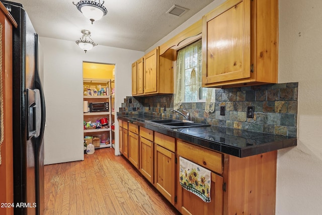 kitchen with sink, a textured ceiling, black fridge with ice dispenser, light wood-type flooring, and decorative backsplash