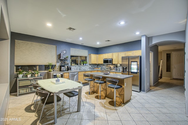 kitchen with a kitchen island, appliances with stainless steel finishes, tasteful backsplash, a breakfast bar area, and light tile patterned floors