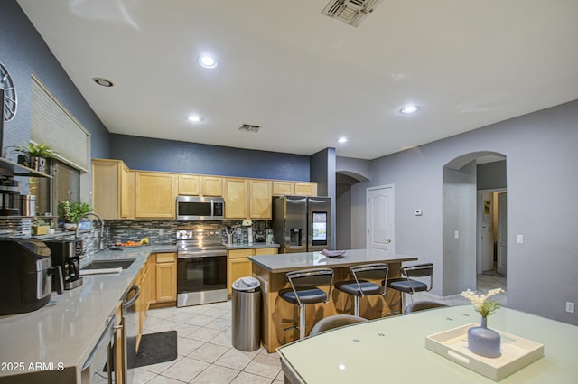 kitchen with light brown cabinetry, sink, tasteful backsplash, a center island, and stainless steel appliances