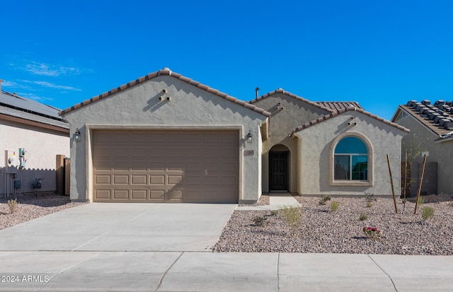 mediterranean / spanish house with stucco siding, an attached garage, fence, driveway, and a tiled roof