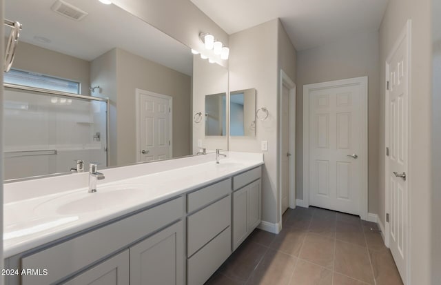 bathroom with double vanity, an enclosed shower, a sink, and tile patterned floors