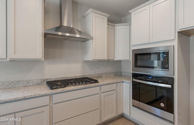 kitchen with light stone countertops, wall chimney exhaust hood, white cabinetry, and stainless steel appliances