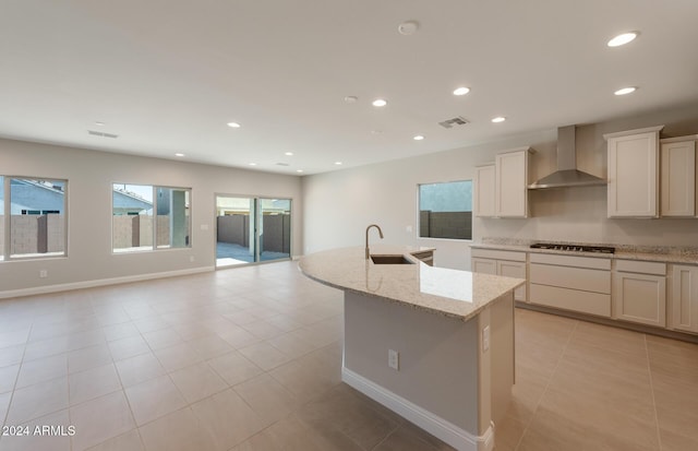 kitchen featuring a center island with sink, visible vents, wall chimney exhaust hood, stainless steel gas cooktop, and a sink