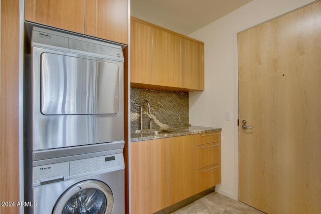 clothes washing area featuring sink, cabinets, and stacked washer / drying machine