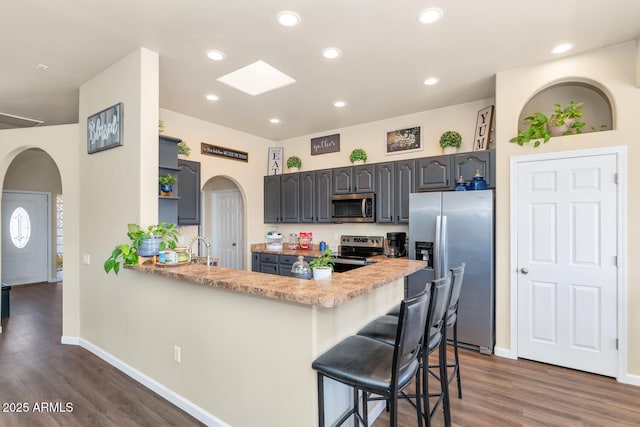 kitchen with arched walkways, a kitchen breakfast bar, a peninsula, stainless steel appliances, and open shelves