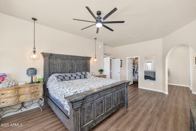 bedroom featuring baseboards, visible vents, arched walkways, wood finished floors, and a spacious closet