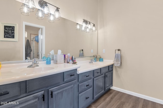 bathroom with a shower with door, double vanity, a sink, wood finished floors, and baseboards