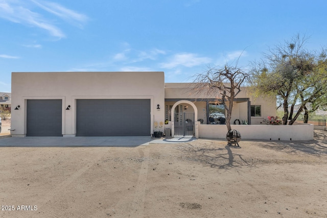 adobe home featuring a fenced front yard, stucco siding, an attached garage, a gate, and driveway