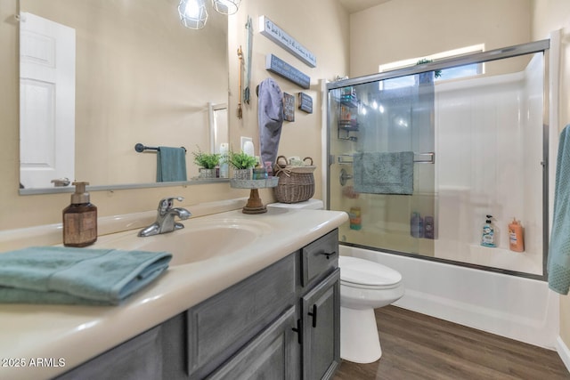 full bath with toilet, bath / shower combo with glass door, wood finished floors, and vanity