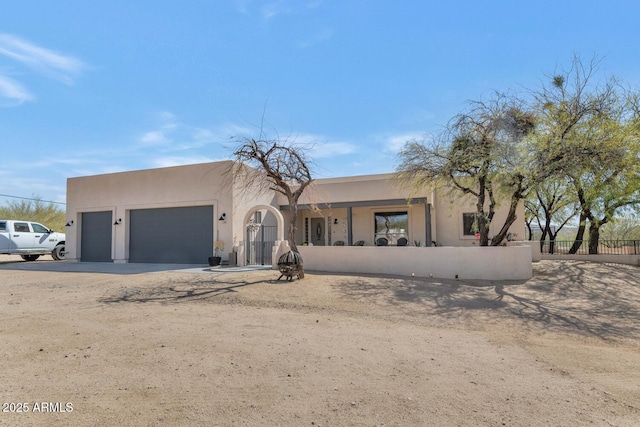 pueblo-style home with an attached garage, driveway, a fenced front yard, and stucco siding