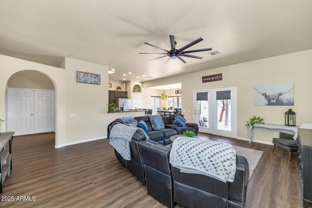 living area with arched walkways, wood finished floors, visible vents, and baseboards