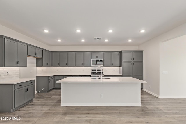 kitchen with stainless steel appliances, sink, light hardwood / wood-style flooring, a kitchen island with sink, and gray cabinetry