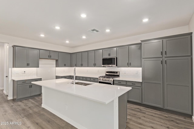 kitchen with stainless steel appliances, sink, hardwood / wood-style floors, gray cabinets, and a center island with sink