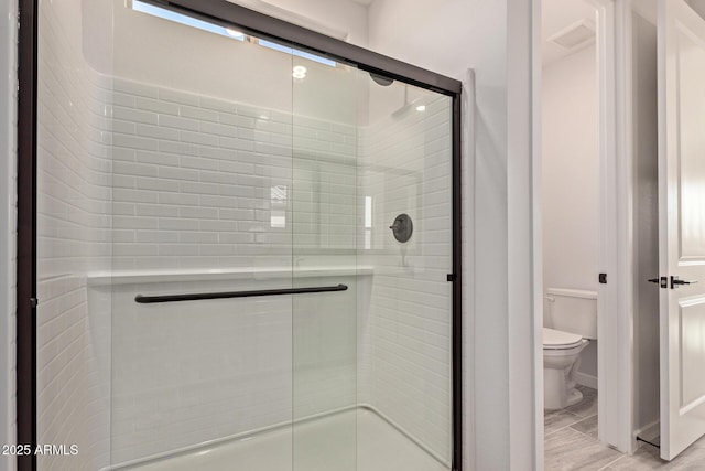 bathroom featuring a shower with shower door and toilet