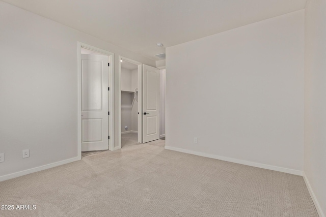 unfurnished bedroom with a walk in closet, light colored carpet, and a closet