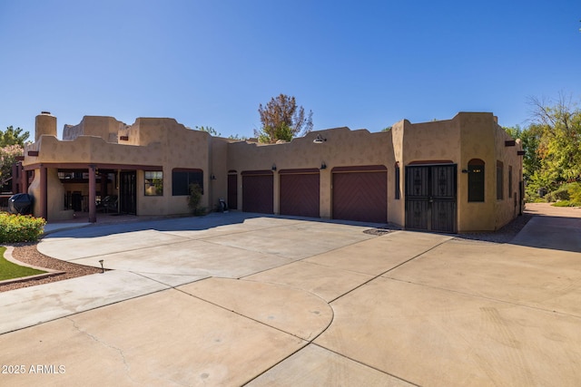 pueblo-style house with an attached garage, concrete driveway, and stucco siding