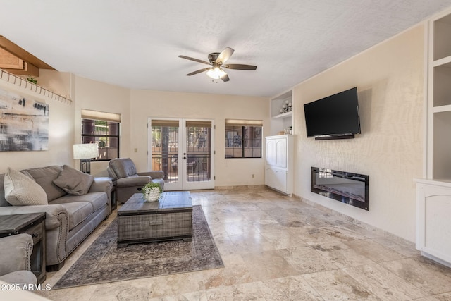 living room featuring ceiling fan, a glass covered fireplace, built in shelves, and french doors