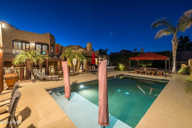 pool at twilight with a patio, a gazebo, and an outdoor pool