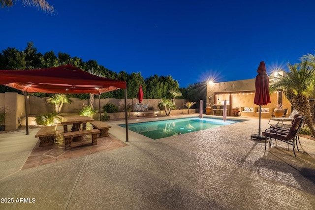 pool at night featuring a patio, a fenced backyard, and a fenced in pool