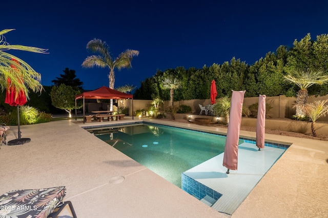pool at night featuring a patio, a fenced backyard, a fenced in pool, and a gazebo