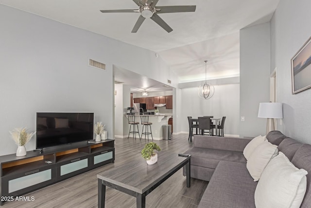 living room with ceiling fan with notable chandelier, vaulted ceiling, wood finished floors, and visible vents