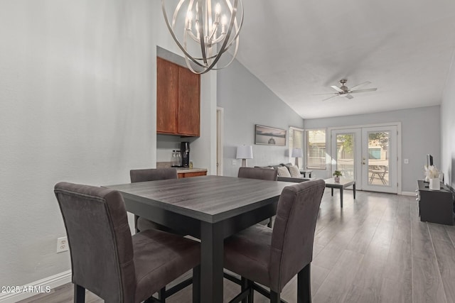 dining room featuring baseboards, french doors, light wood-type flooring, high vaulted ceiling, and ceiling fan with notable chandelier