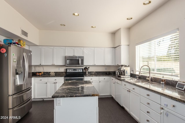 kitchen with dark stone counters, sink, appliances with stainless steel finishes, a kitchen island, and white cabinetry