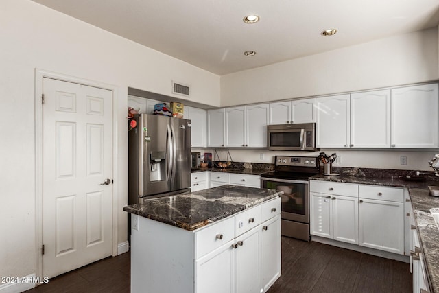 kitchen featuring dark wood-type flooring, stainless steel appliances, a kitchen island, dark stone countertops, and white cabinets