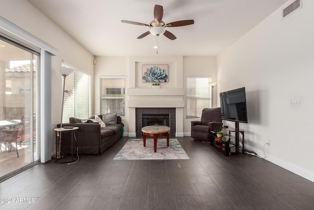 living room featuring a tiled fireplace, ceiling fan, dark wood-type flooring, and a healthy amount of sunlight