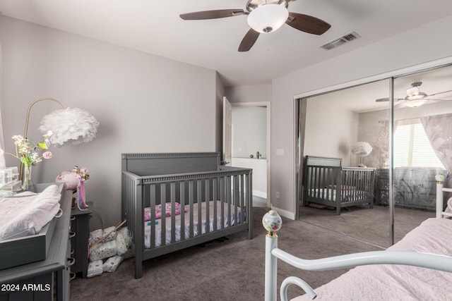 bedroom with ceiling fan, dark carpet, a crib, and a closet