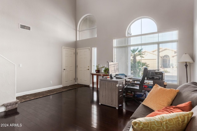 office space featuring a healthy amount of sunlight, dark hardwood / wood-style flooring, and a towering ceiling