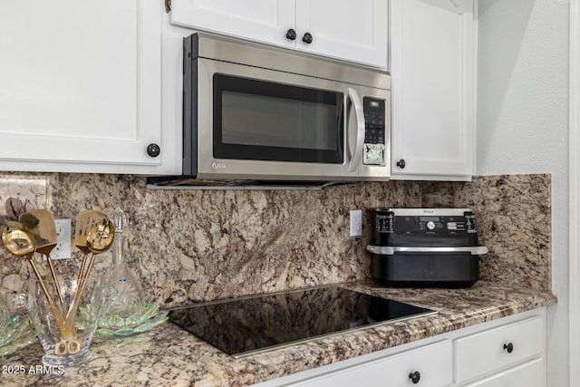 6941 W Voltaire Ave, Peoria, AZ 85381 - kitchen featuring stainless steel microwave, black electric stovetop, white cabinets, and tasteful backsplash