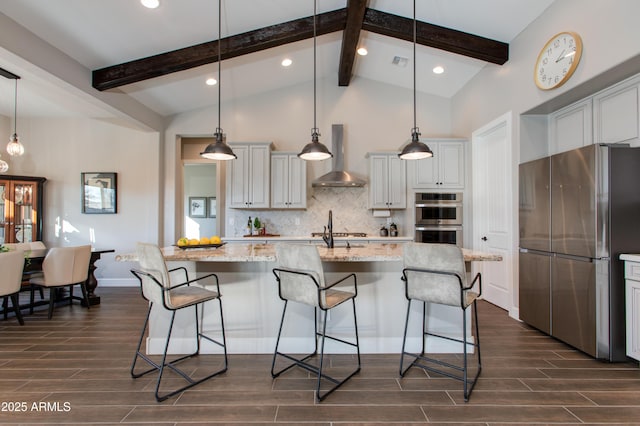 kitchen featuring decorative backsplash, appliances with stainless steel finishes, light stone counters, wall chimney exhaust hood, and an island with sink