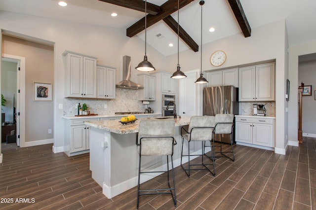 kitchen featuring wall chimney exhaust hood, beam ceiling, a center island with sink, hanging light fixtures, and a breakfast bar area