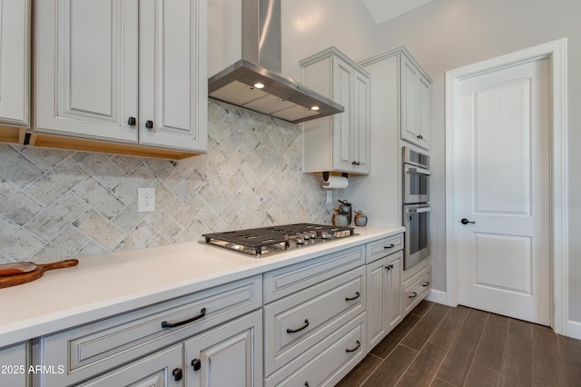 kitchen featuring tasteful backsplash, white cabinets, wall chimney range hood, and appliances with stainless steel finishes