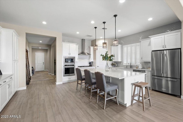 kitchen featuring white cabinetry, appliances with stainless steel finishes, wall chimney range hood, and decorative light fixtures