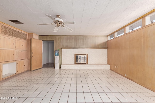 unfurnished living room featuring ceiling fan, light tile patterned floors, a fireplace, and wood walls