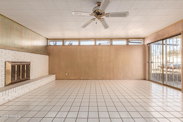 unfurnished living room with light tile patterned floors, a fireplace, ceiling fan, and wood walls