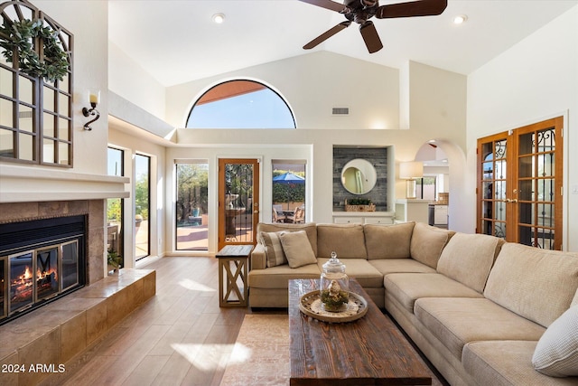 living room featuring ceiling fan, french doors, light hardwood / wood-style flooring, high vaulted ceiling, and a fireplace