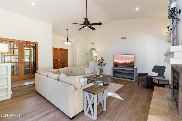 living room with french doors, ceiling fan, hardwood / wood-style flooring, high vaulted ceiling, and a fireplace