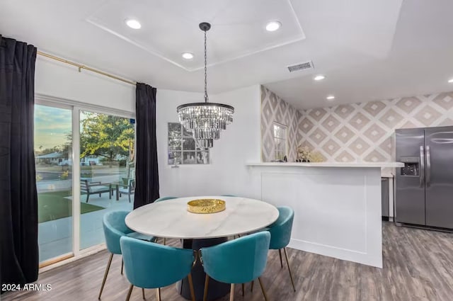 dining area with a notable chandelier, wood-type flooring, and a tray ceiling