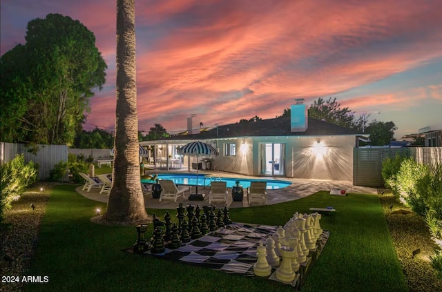 back house at dusk featuring a patio, a fenced in pool, and a yard