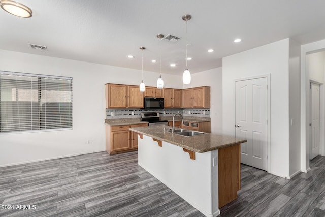 kitchen featuring stainless steel range with electric cooktop, a center island with sink, sink, hanging light fixtures, and tasteful backsplash