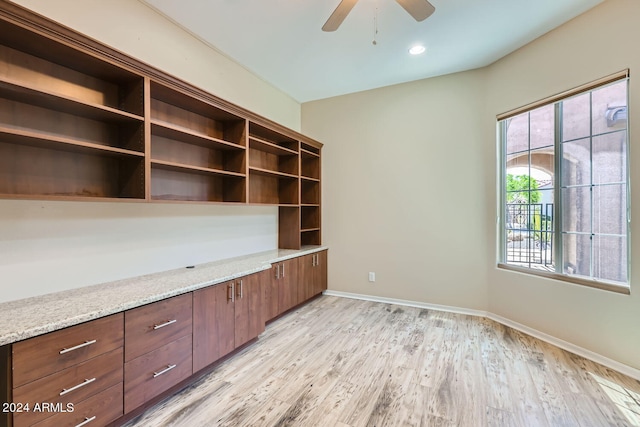 unfurnished office featuring built in desk, light wood-type flooring, and ceiling fan