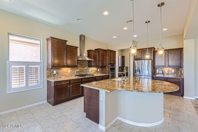 kitchen with pendant lighting, a kitchen island with sink, wall chimney range hood, decorative backsplash, and stainless steel appliances