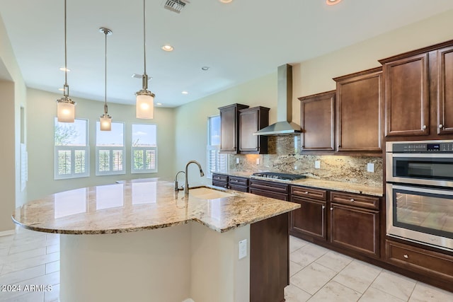 kitchen featuring decorative light fixtures, a center island with sink, wall chimney exhaust hood, and sink