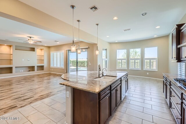 kitchen with an island with sink, dark brown cabinets, light hardwood / wood-style flooring, decorative light fixtures, and sink