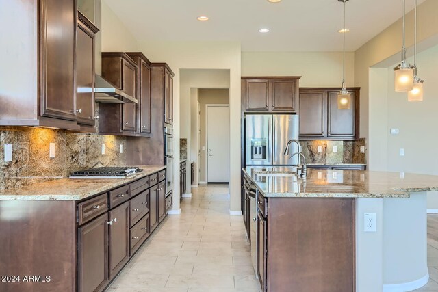 kitchen with light stone counters, appliances with stainless steel finishes, decorative light fixtures, and sink